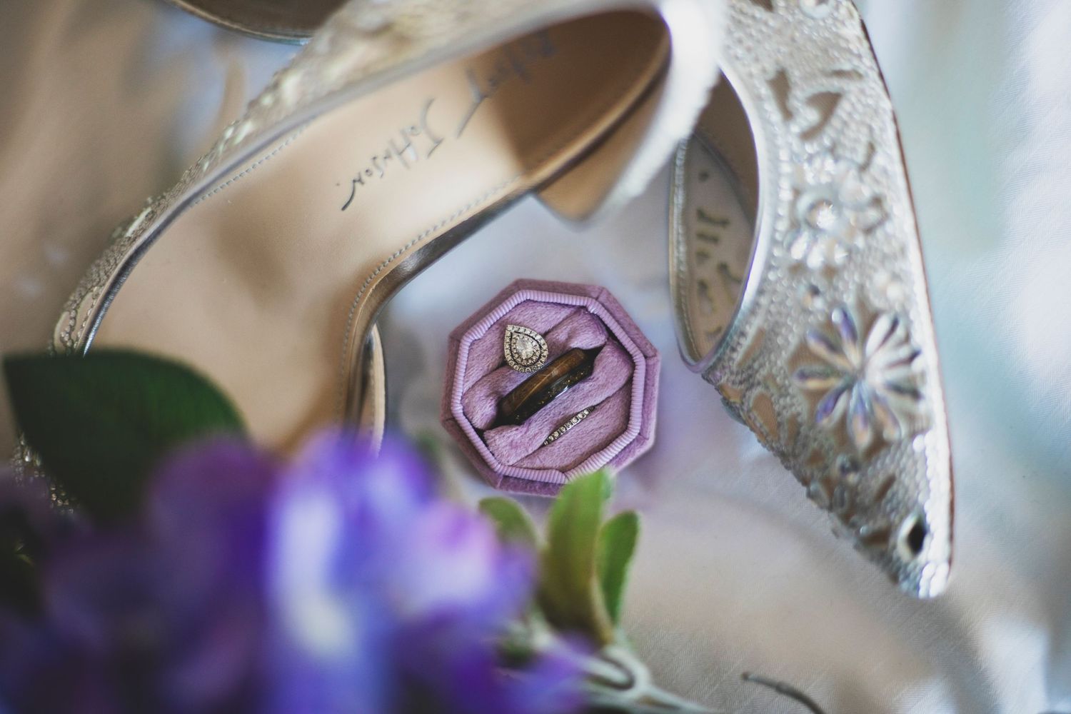 Close-up detail of crystal wedding shoes with purple flowers in soft focus.