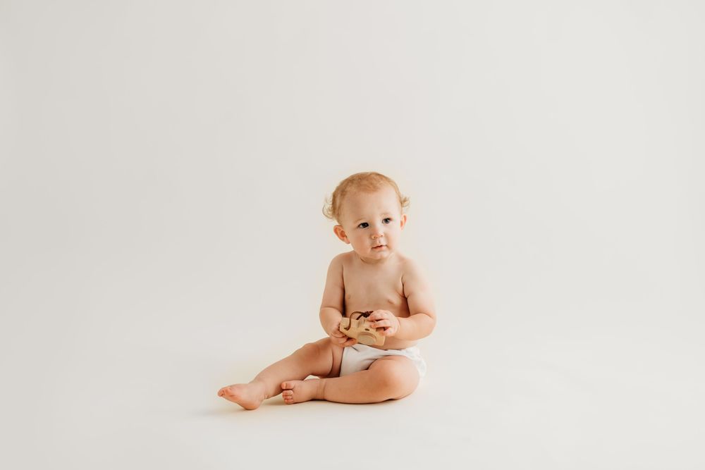 Baby in white diaper sitting on floor during minimalist studio portrait session.