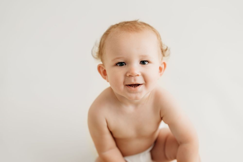 Baby in diaper smiling joyfully against white background during professional photoshoot.