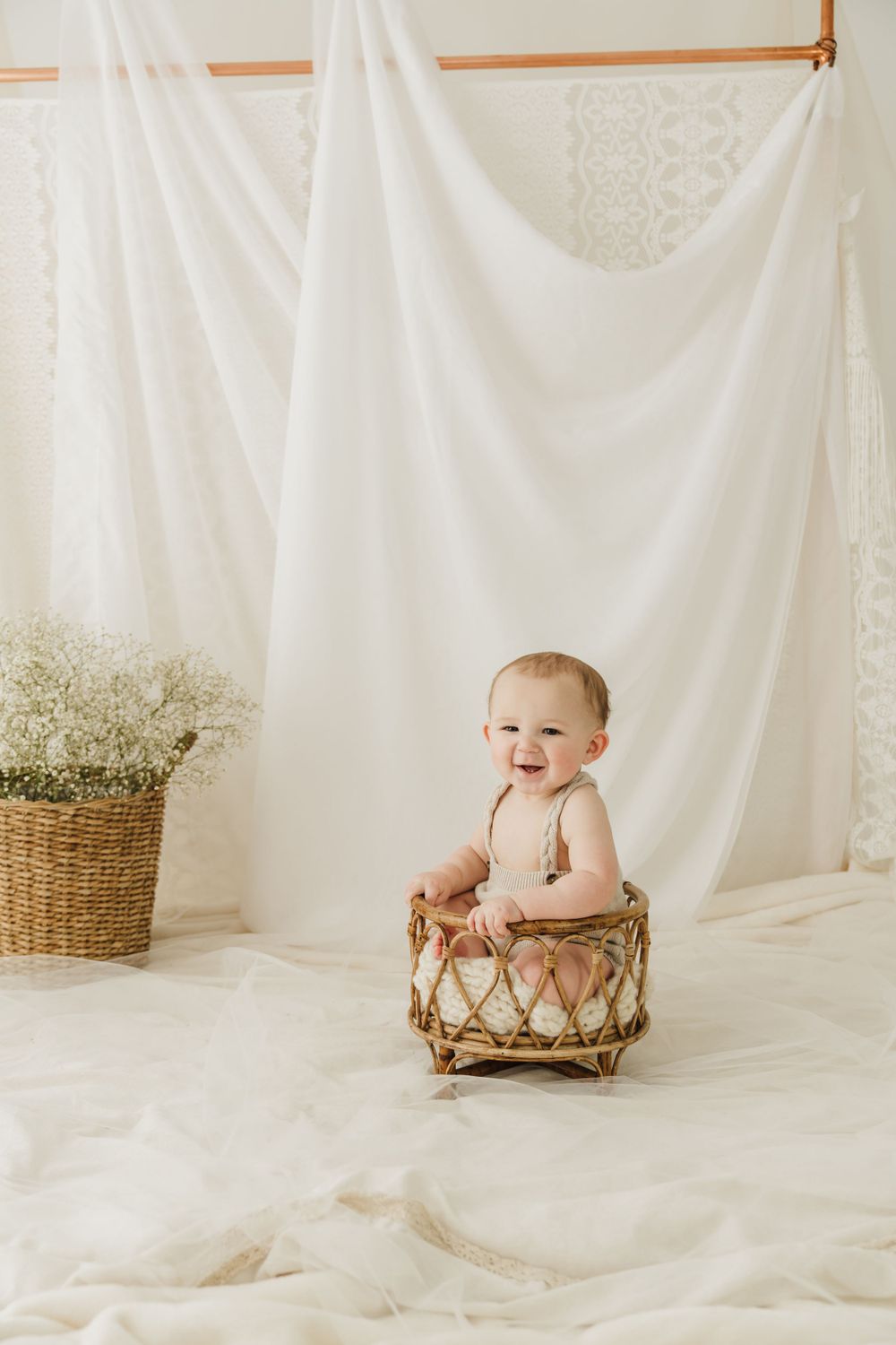 Baby sitting in woven basket against white backdrop with baby's breath flowers.