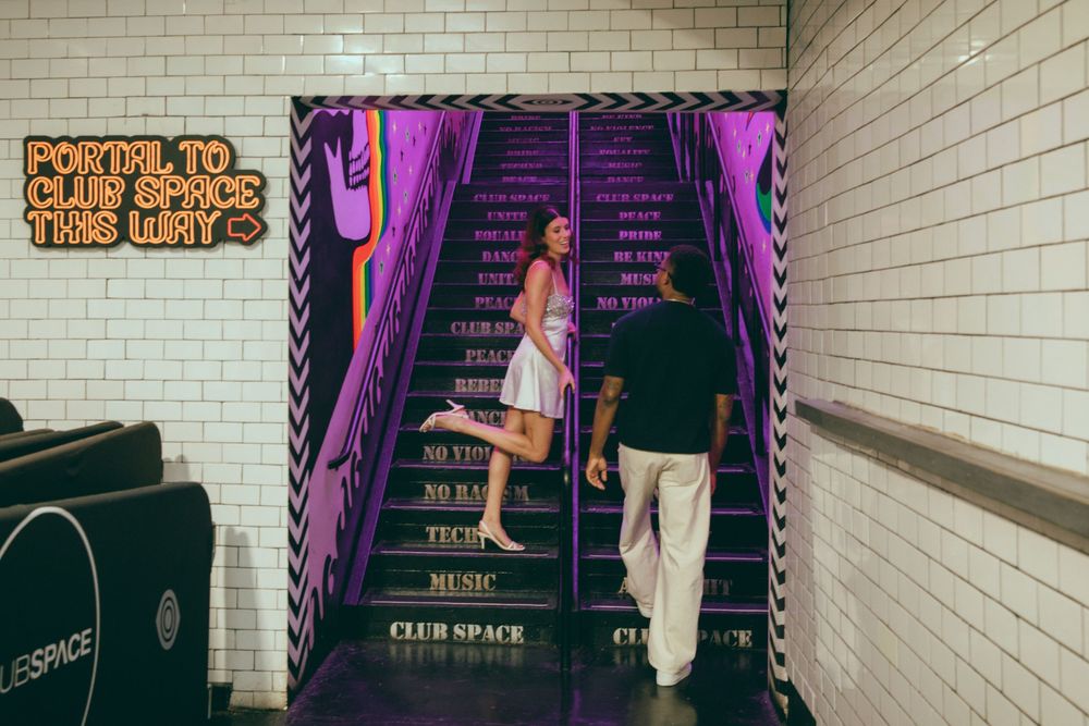Two people on purple neon-lit stairs at Club Space entrance with colorful signage in an urban subway setting.