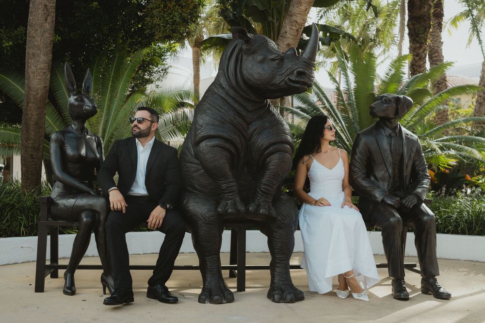 Couple posing among black animal statues including a boar and rabbit in a tropical garden setting.