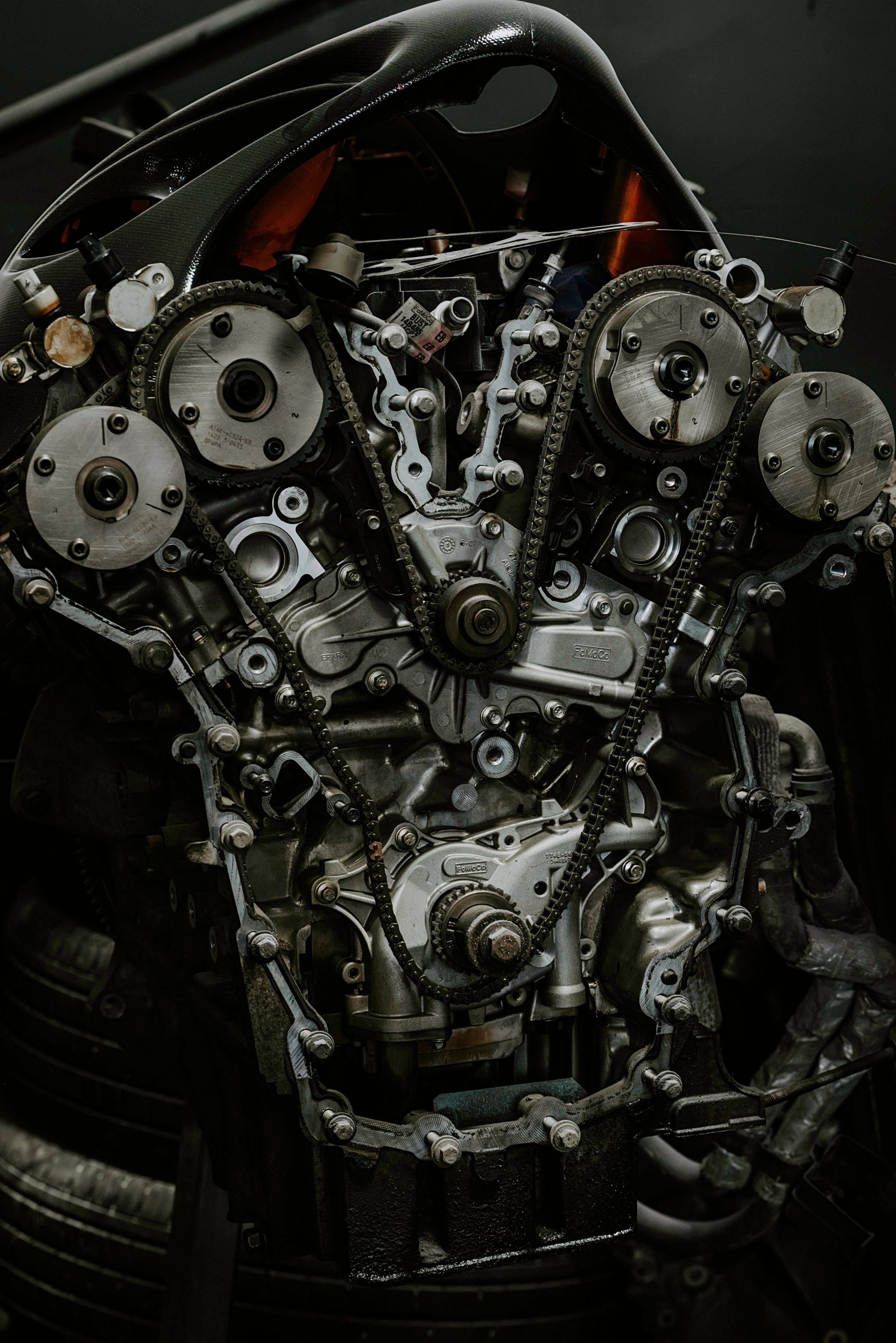 Close-up view of a complex automobile engine showing timing belts, gears, and mechanical components in dark lighting.