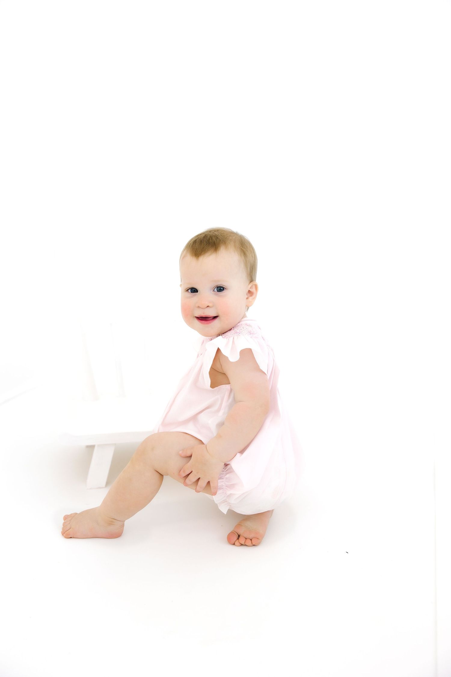 Baby in pink outfit sits on white floor.