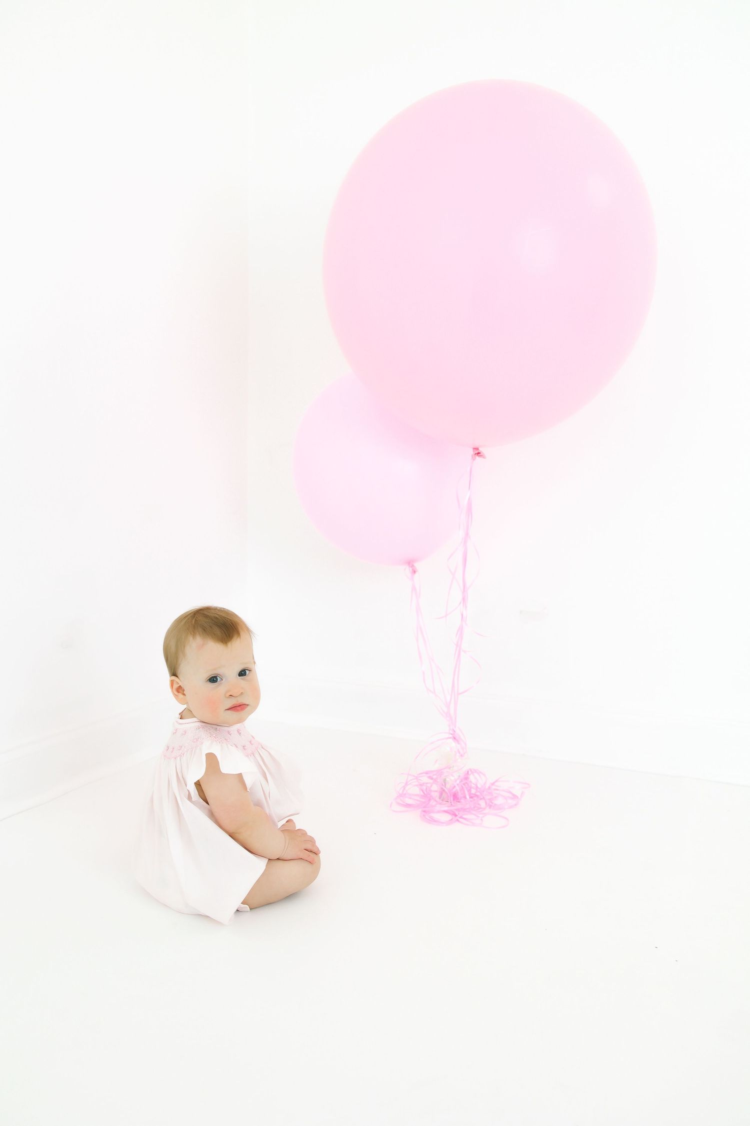 Baby crawling on white floor with pink balloon in background.
