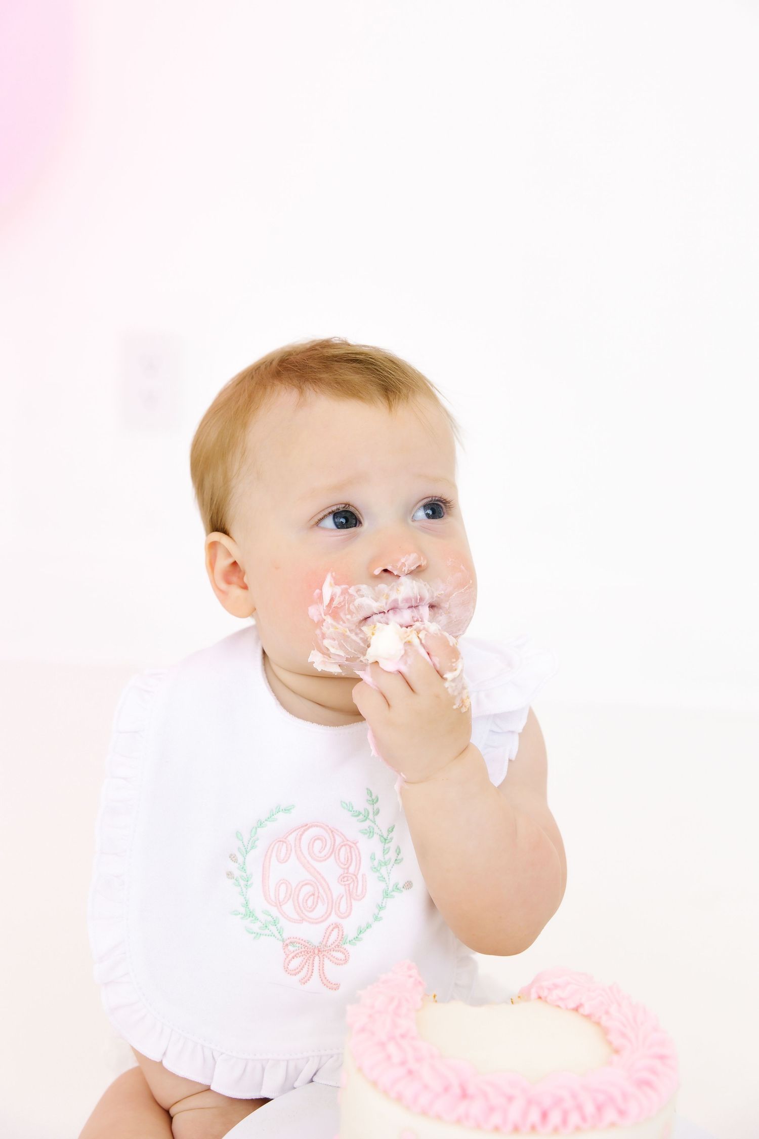 Baby with cake frosting on face during cake smash photoshoot with pink accents.