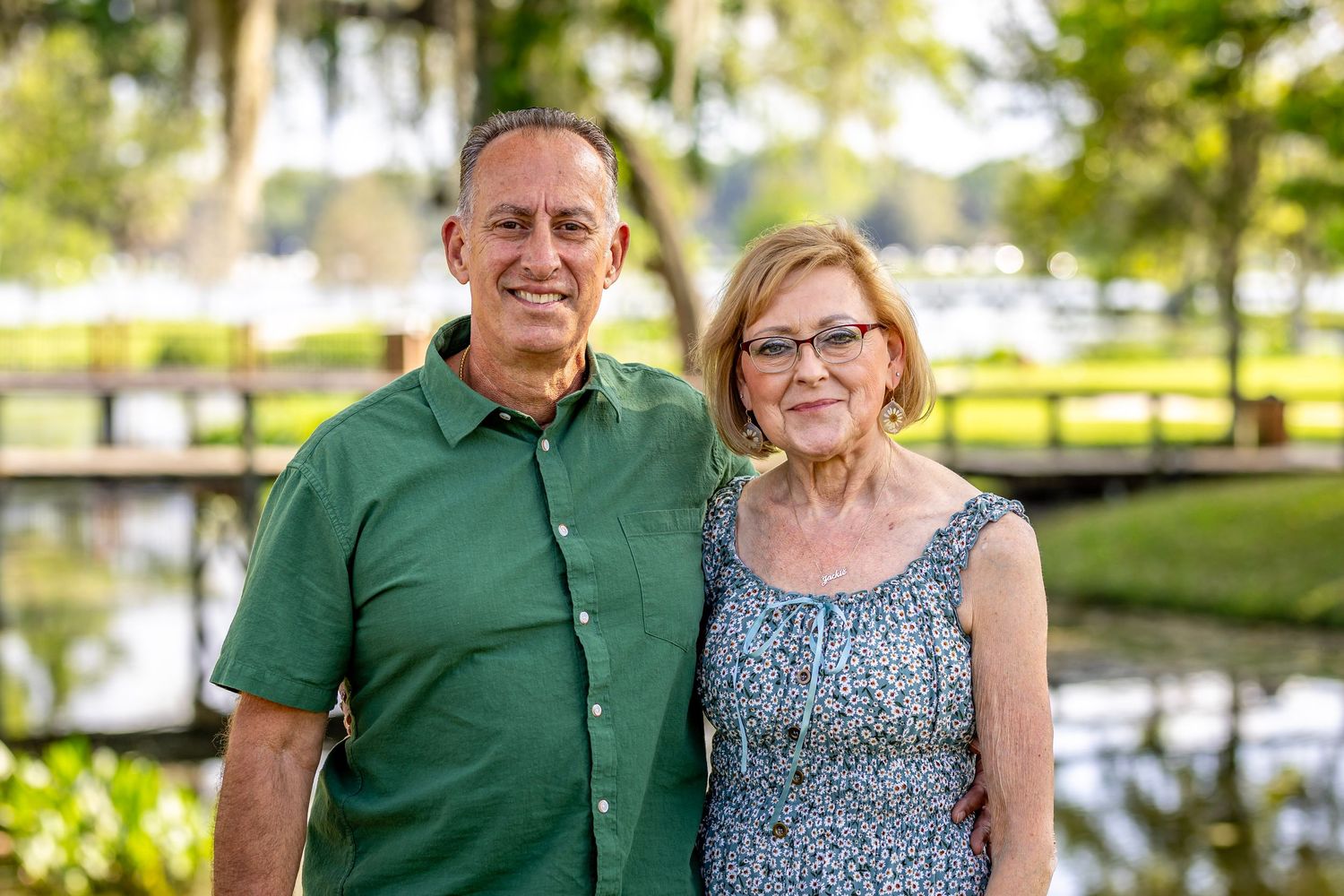 Mature couple posing outdoors in casual attire near water.