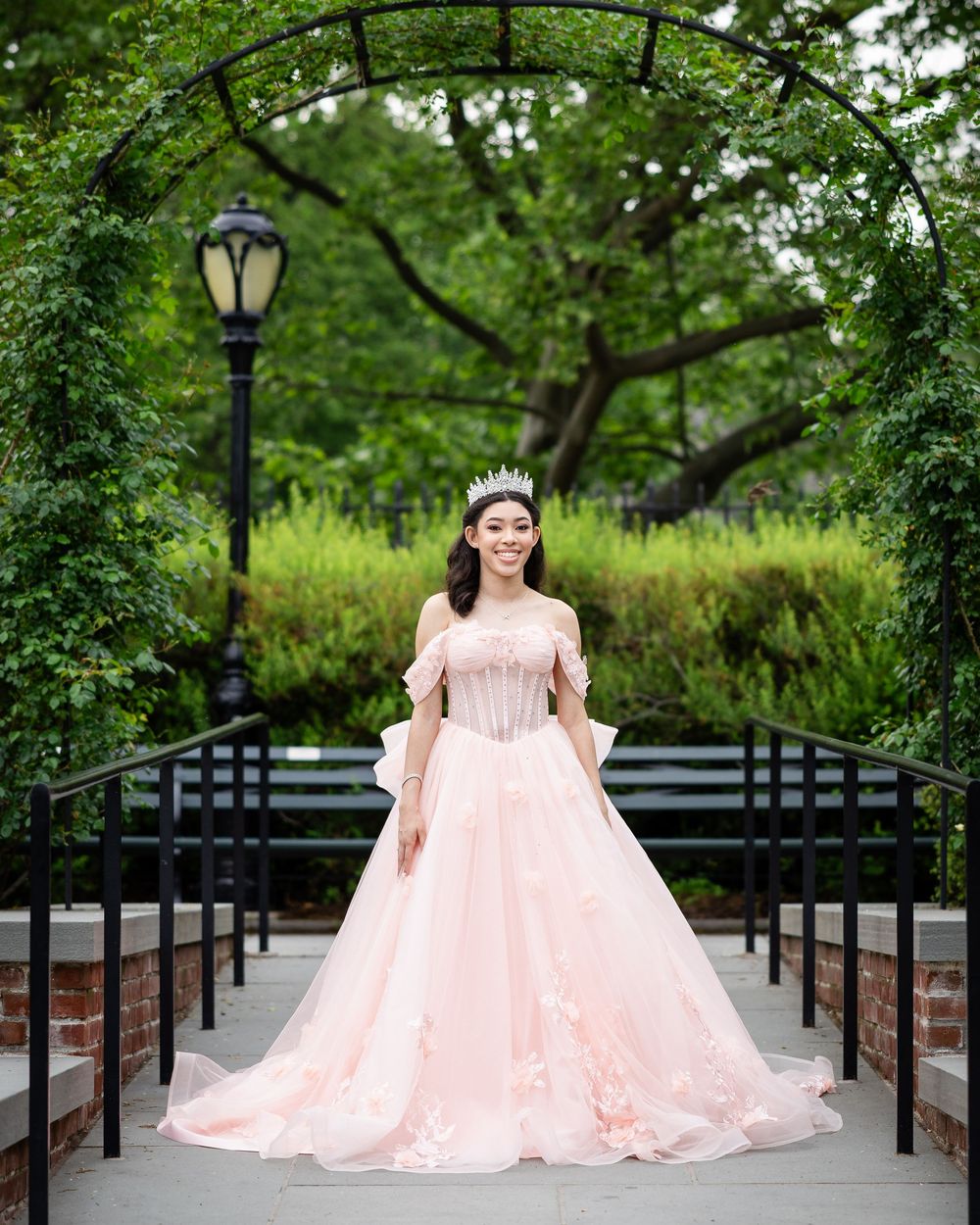 Romantic outdoor photo in a pink ballgown under a garden archway with lamp post.