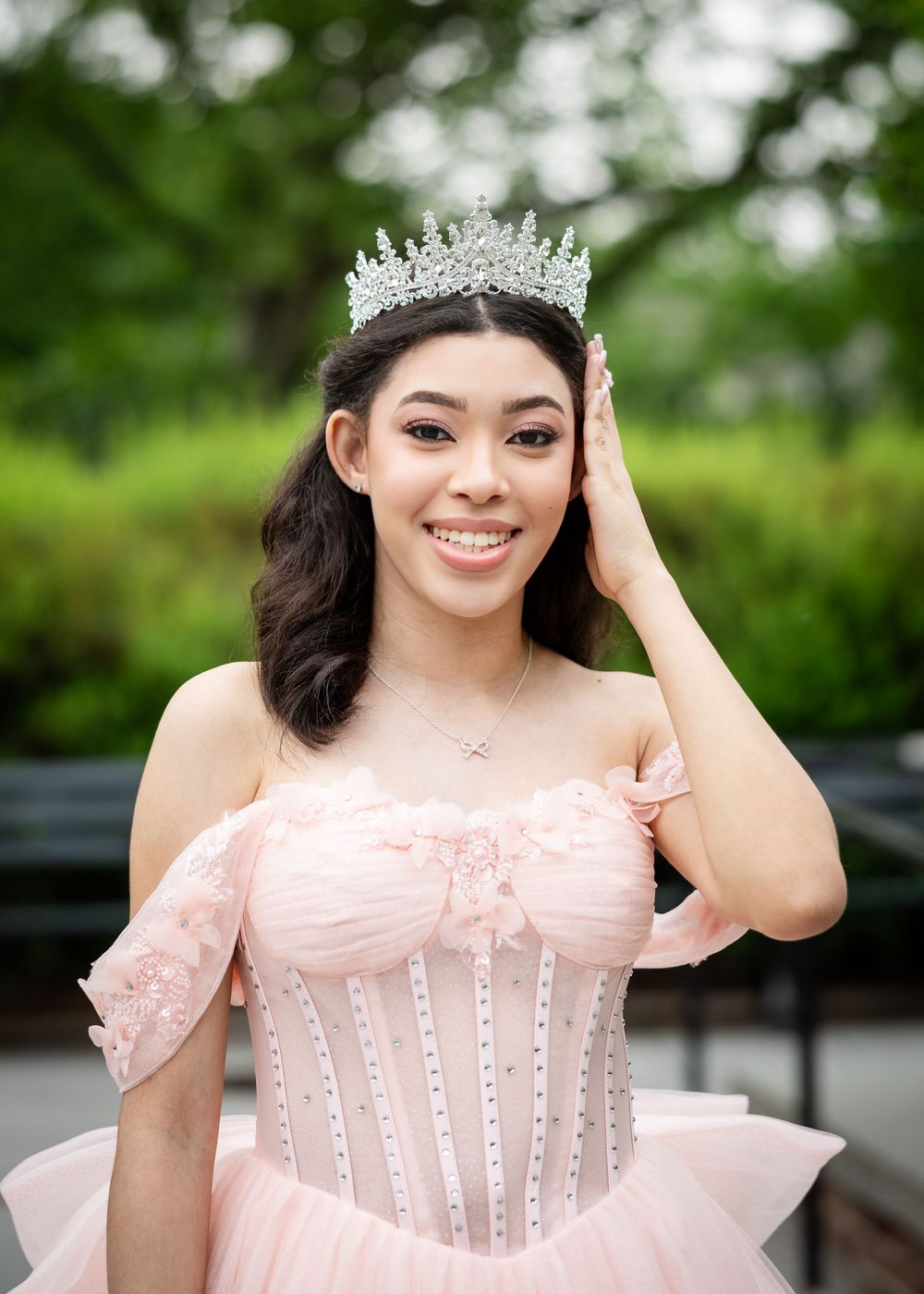 Close-up outdoor portrait wearing sparkly crown and pink off-shoulder gown.
