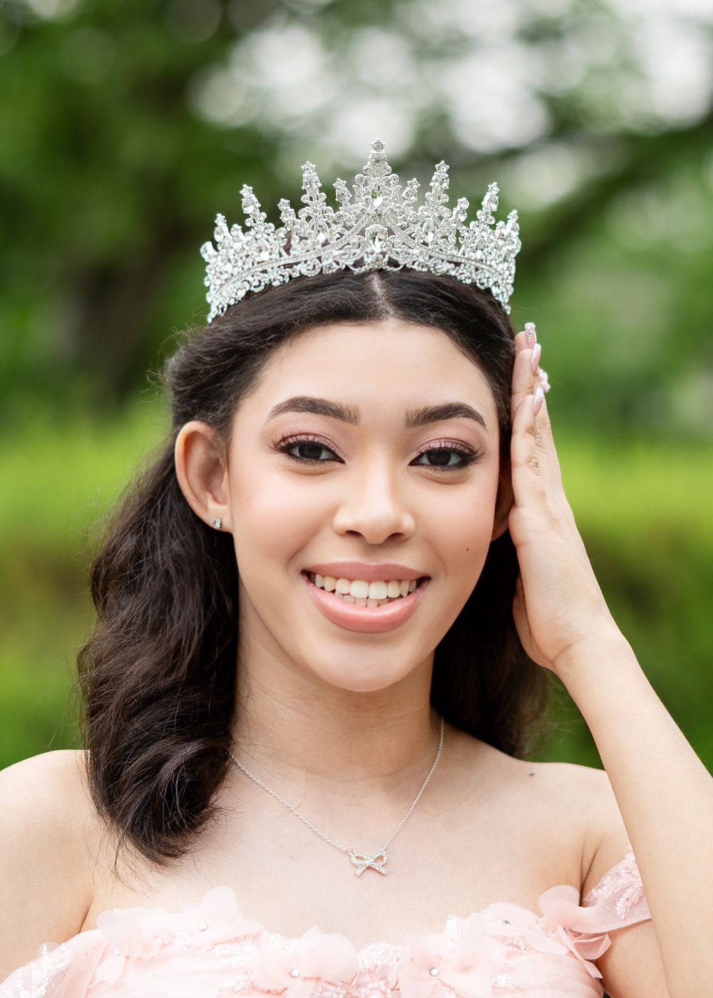 Close-up portrait showcasing intricate crystal crown and pink off-shoulder dress details.