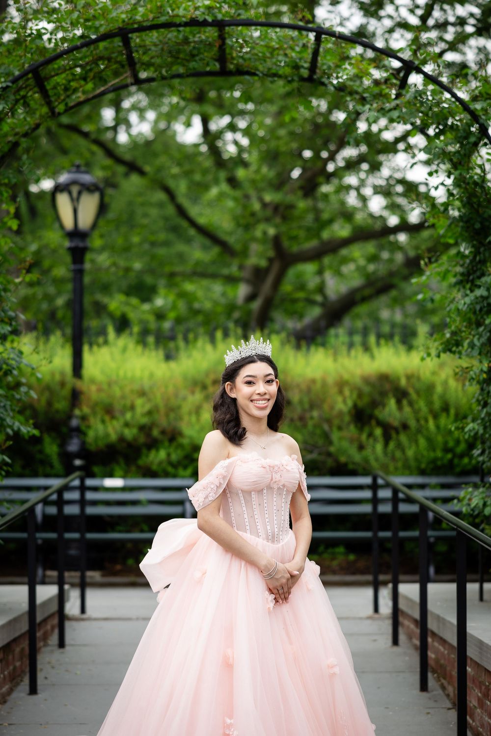 A princess-style pink tulle gown photographed in a park setting with greenery and lamp posts.