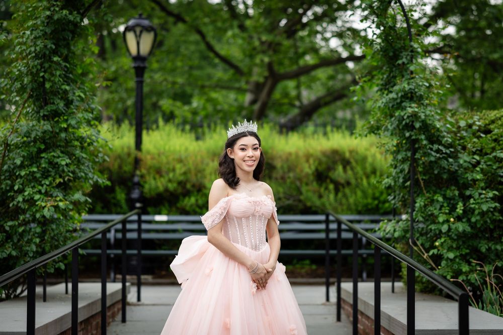 A flowing pink ballgown with off-shoulder details photographed on a garden pathway.