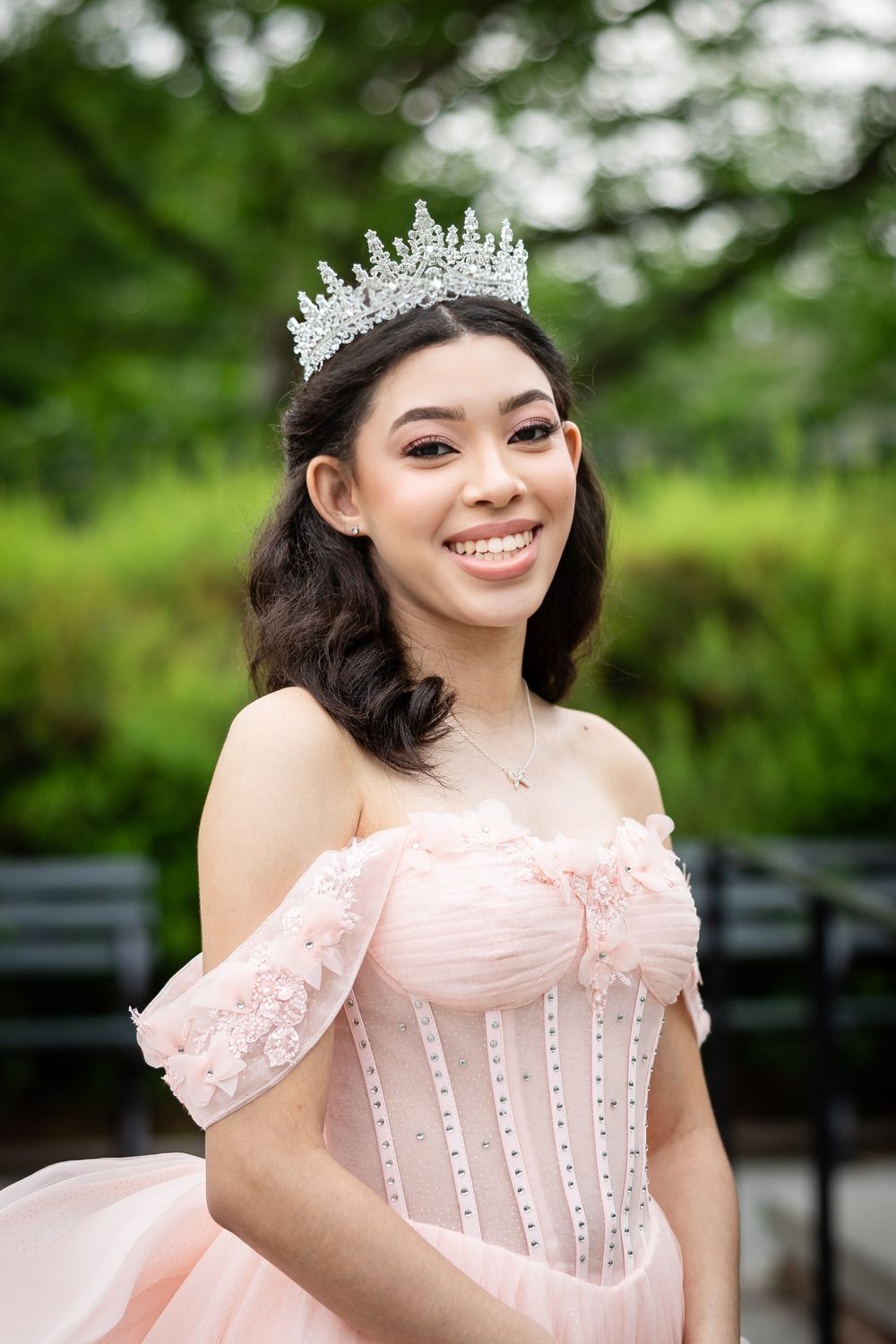 An elegant pink corset gown with crystal crown photographed in a lush outdoor setting.