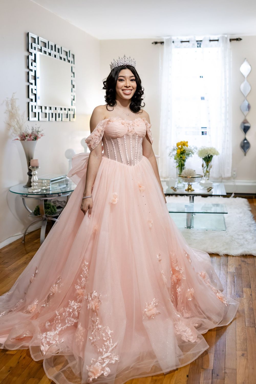 Full-length view of a blush pink ball gown with corset top and floral appliques in a bright room.