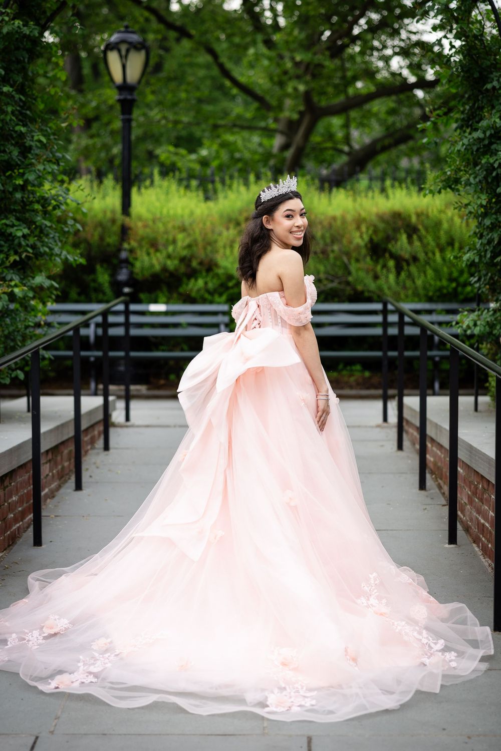 A princess ball gown with dramatic train photographed on a park walkway surrounded by greenery.