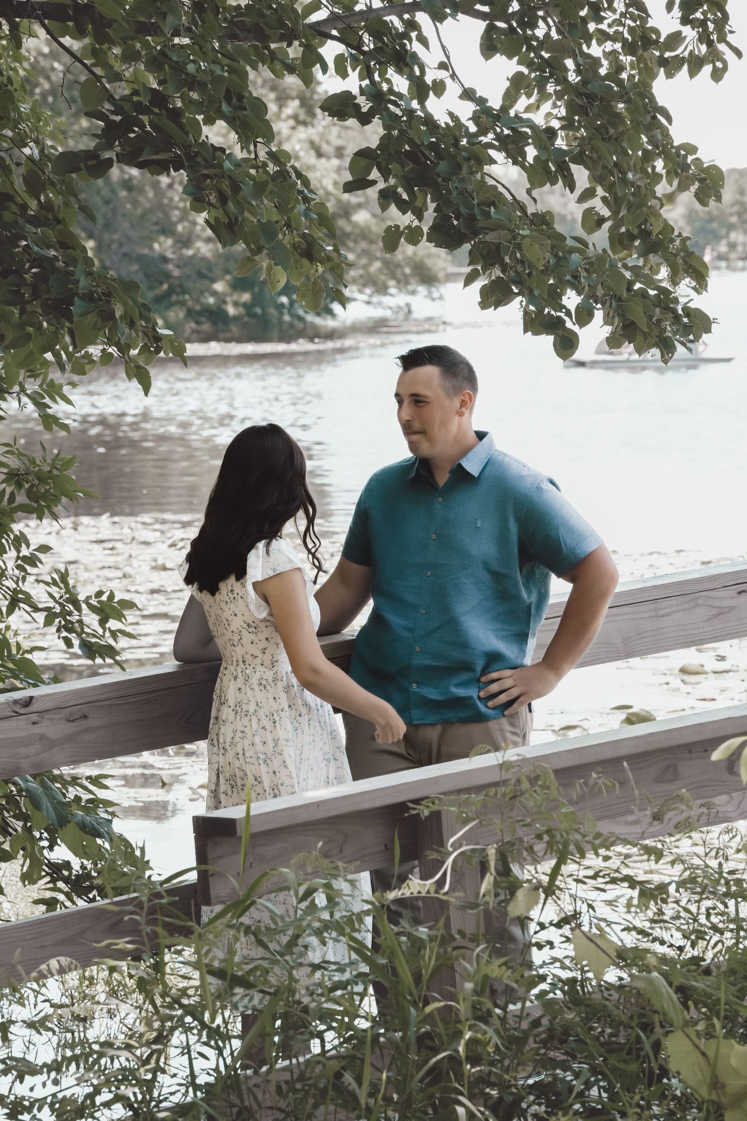 Casual couple enjoys conversation while sitting on wooden railing by a serene lake.