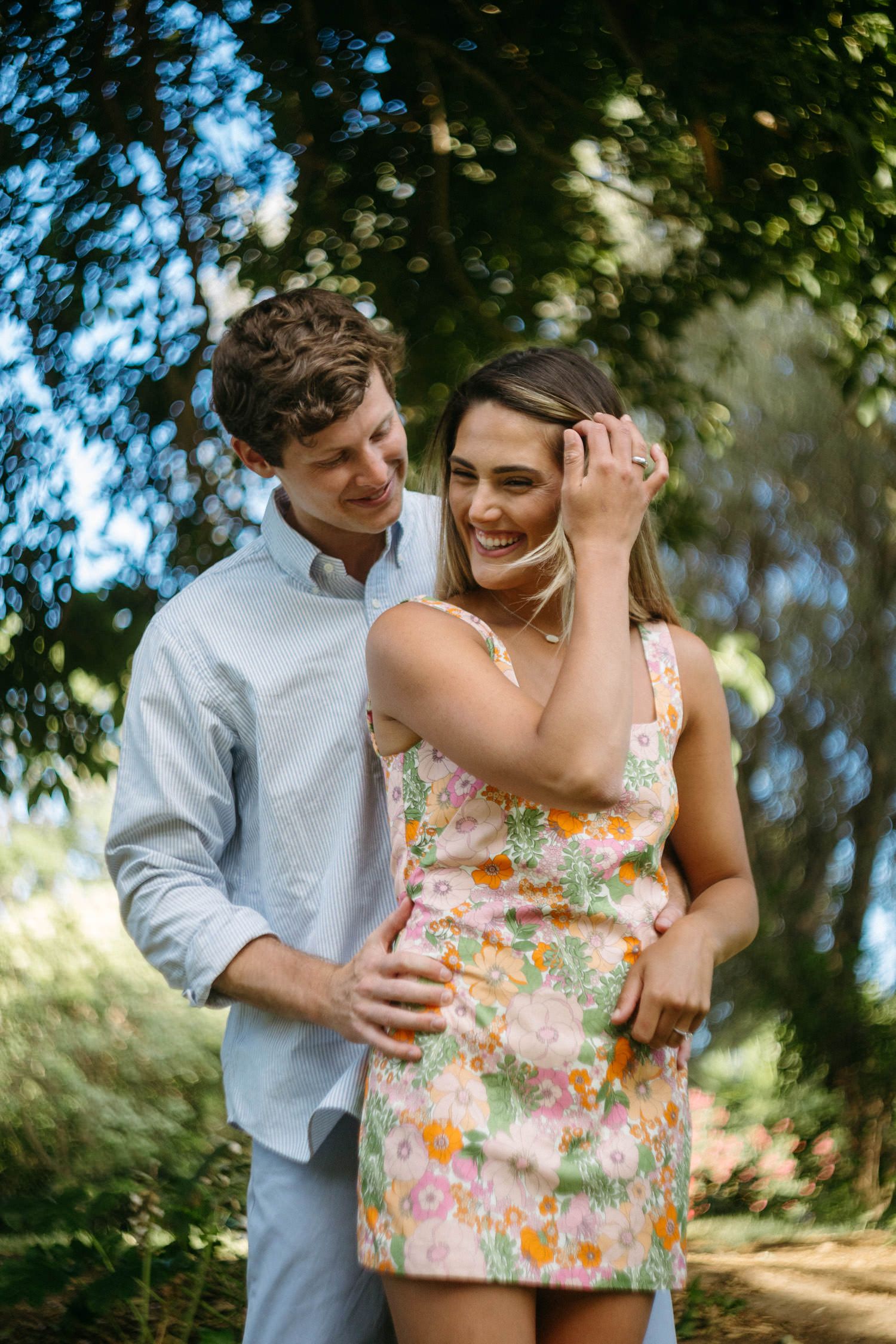 Couple sharing joyful moments in dappled sunlight under trees.