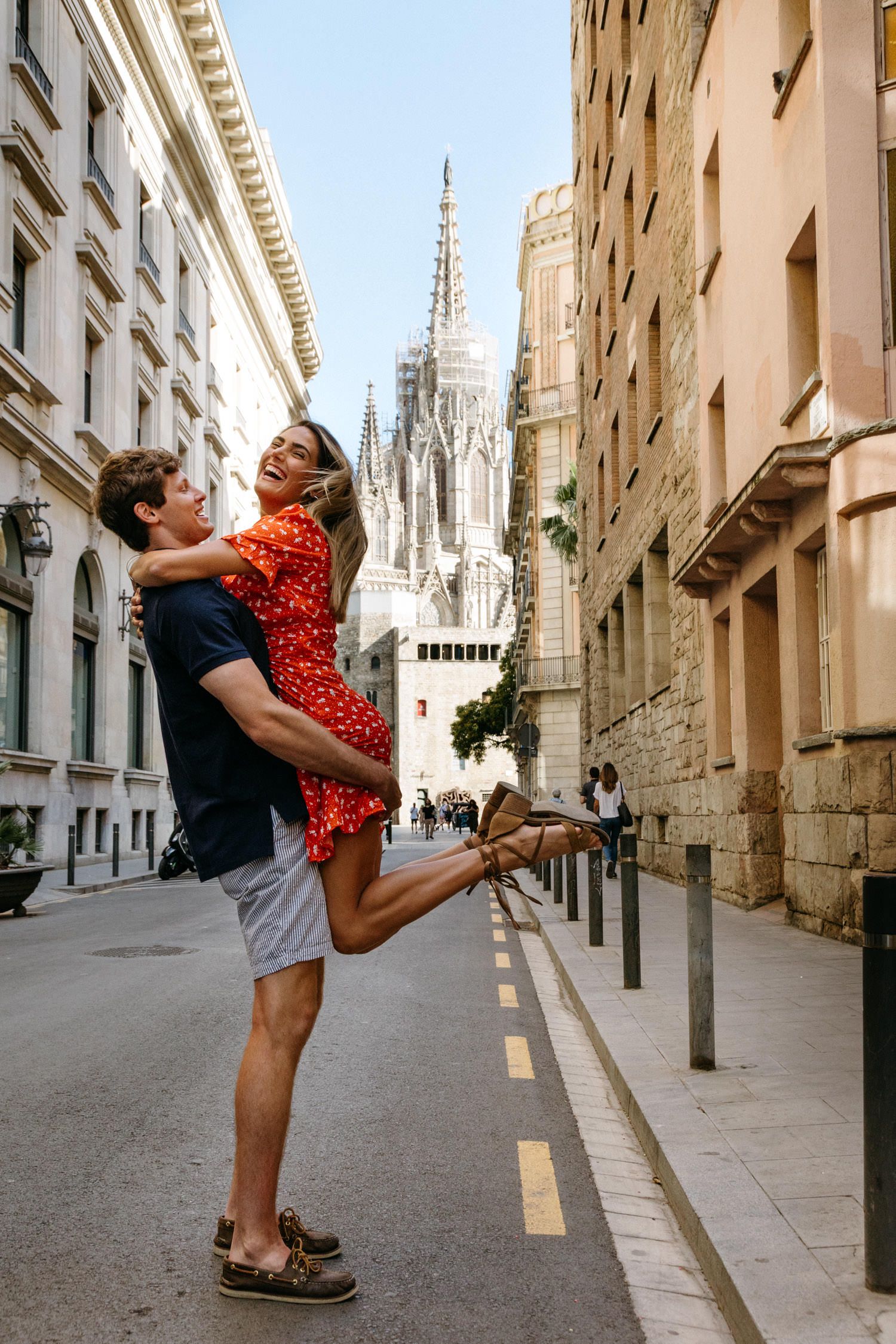 Playful couple dancing in a European street with Gothic architecture in the background.
