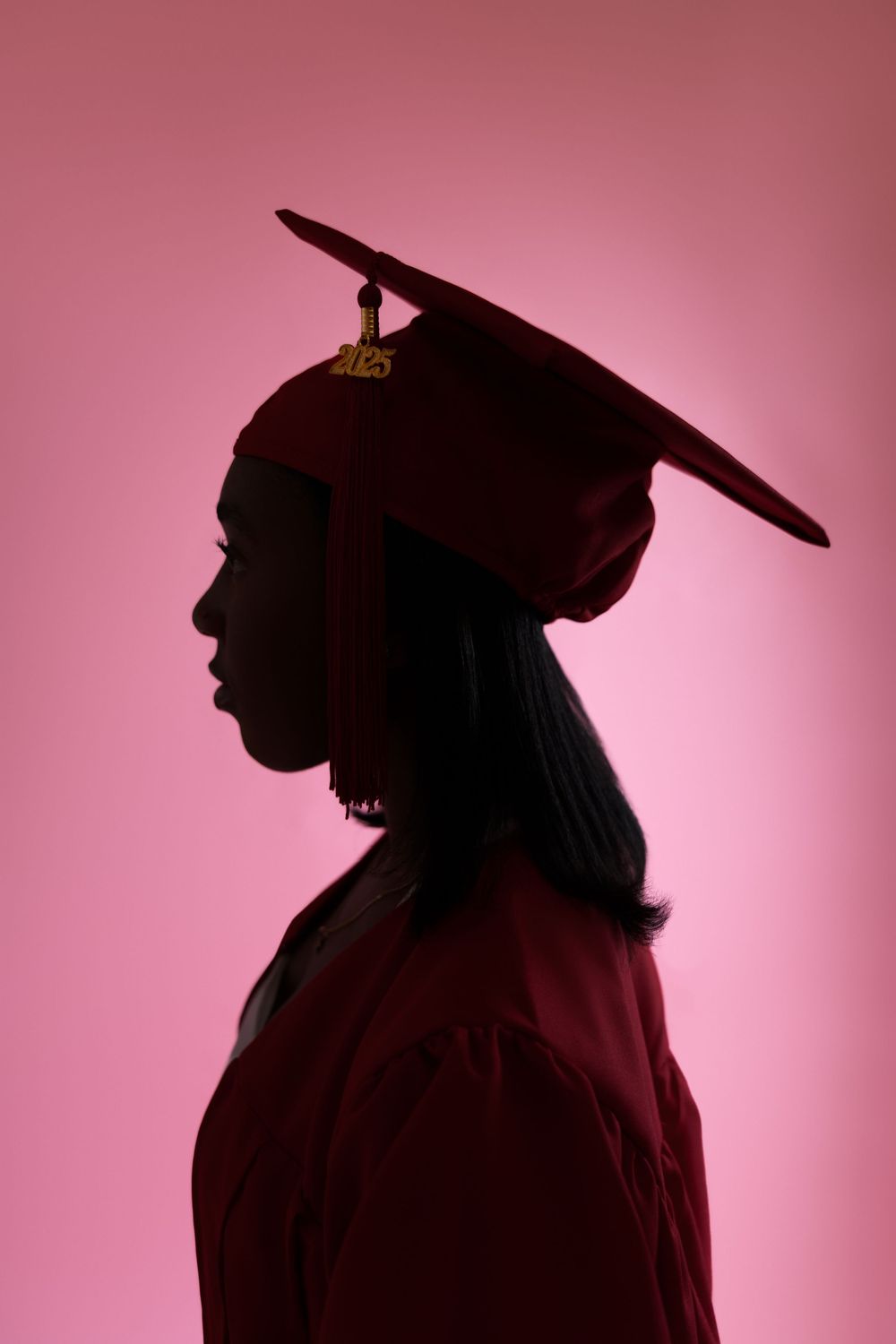 Silhouette profile of a graduate in cap and gown against a pink background.