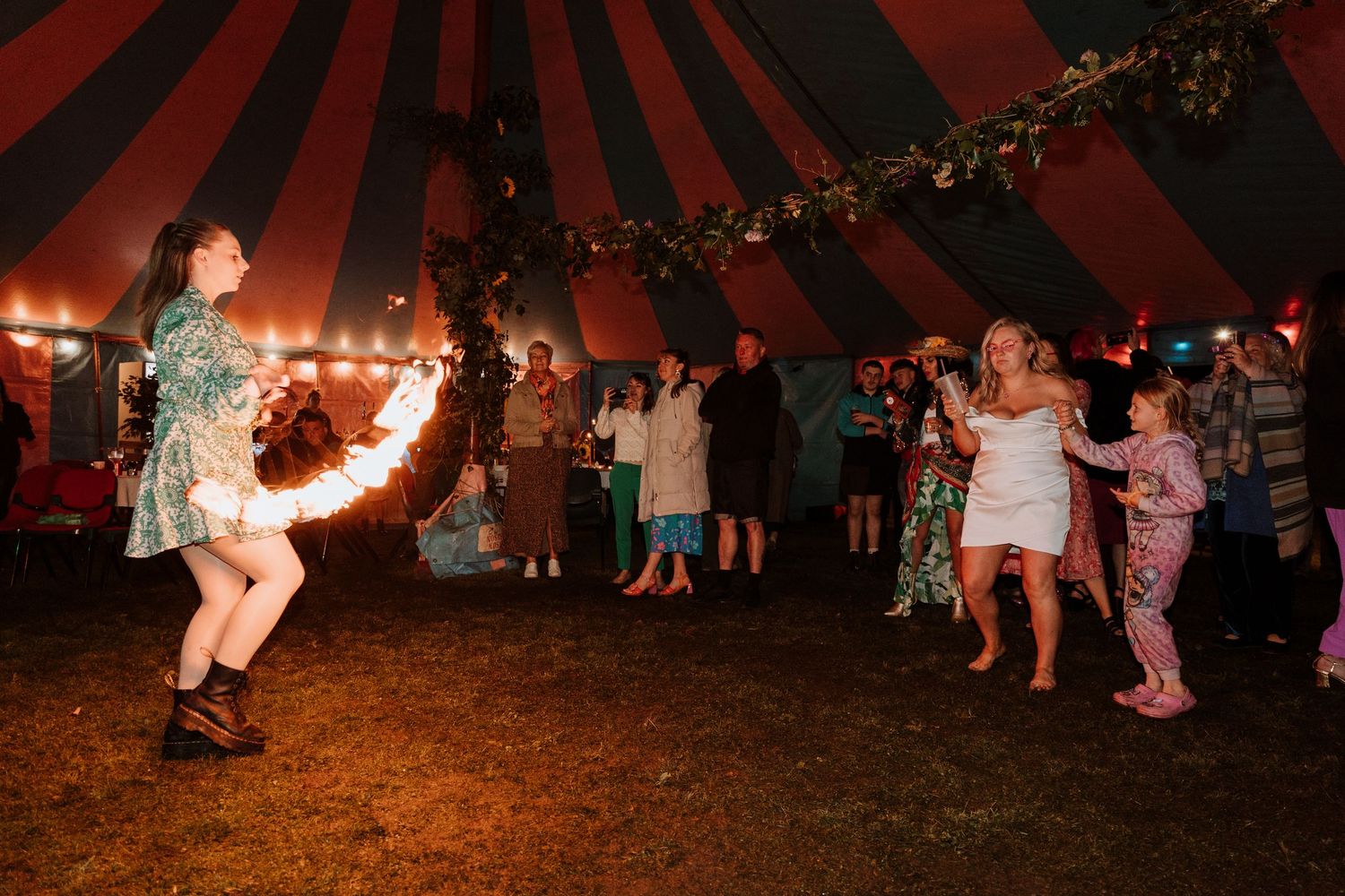 Wedding under a large red and white striped tent during an evening wedding reception watching fire dancer