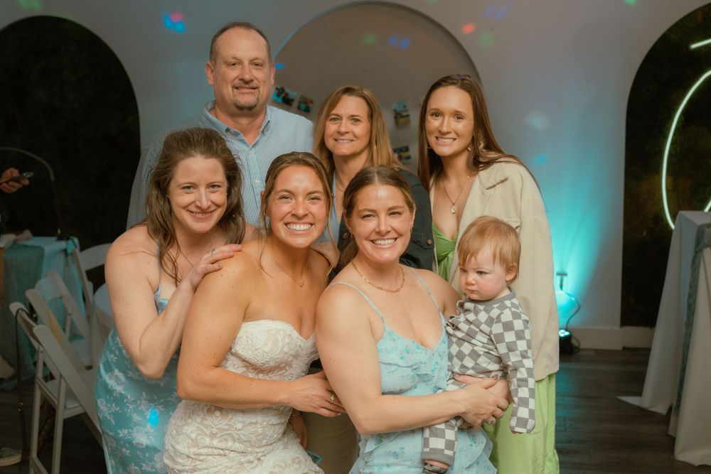 Wedding celebration with guests gathered for a group photo in a venue with blue lighting and festive atmosphere.