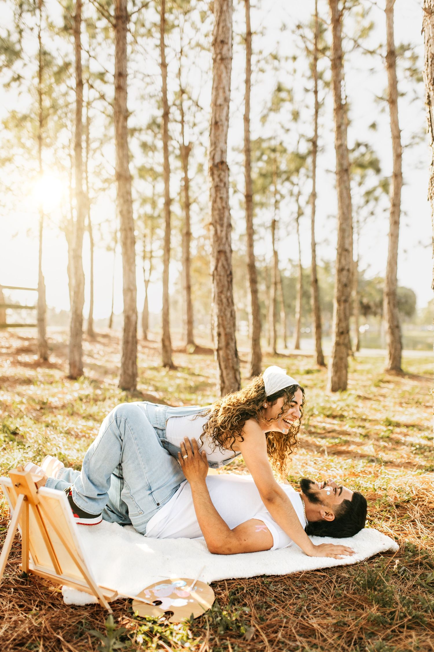 Romantic picnic scene in sunny pine forest with couple laying on blanket.