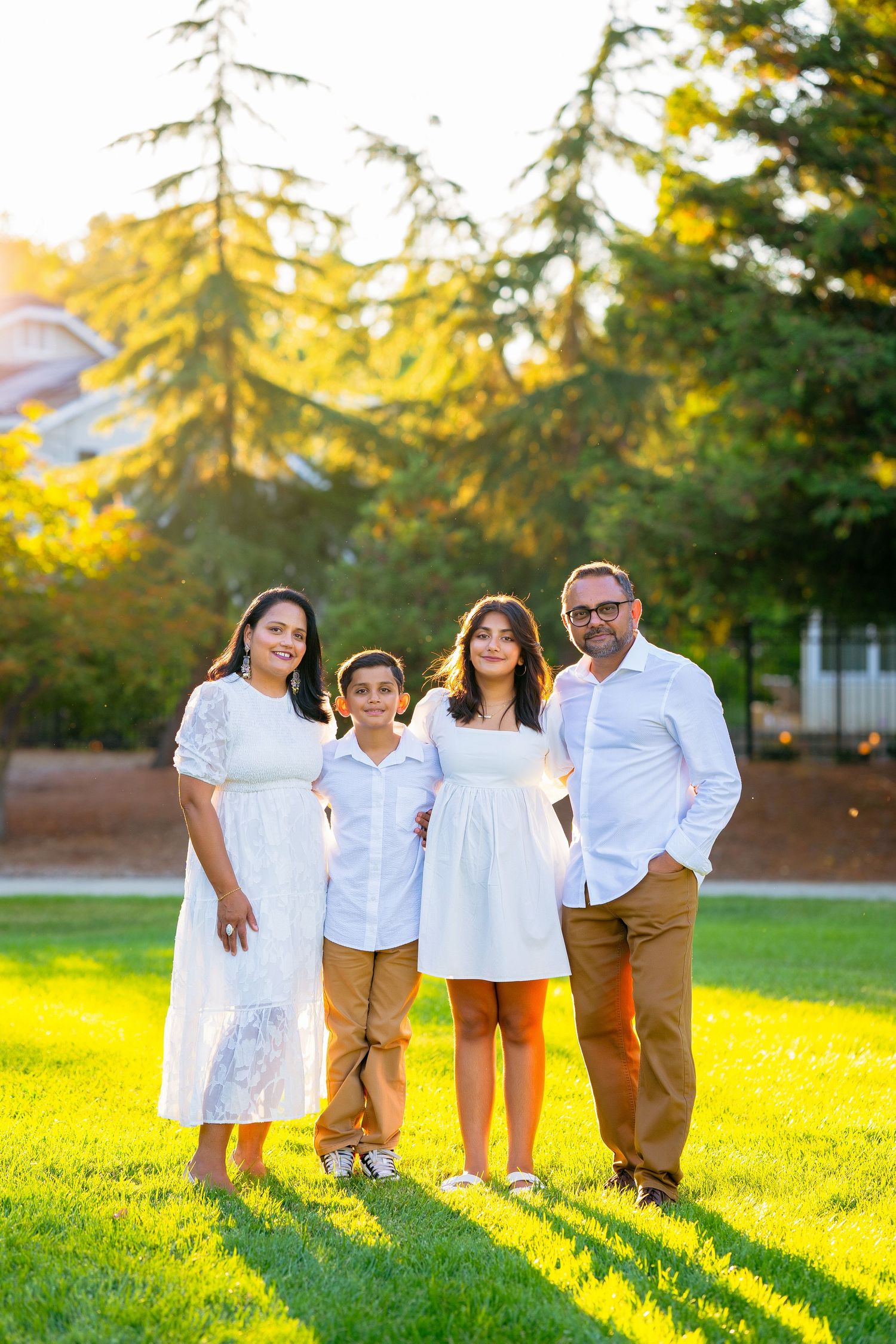 A happy family in white shirts and khaki pants poses together on a sunlit grassy field during golden hour.