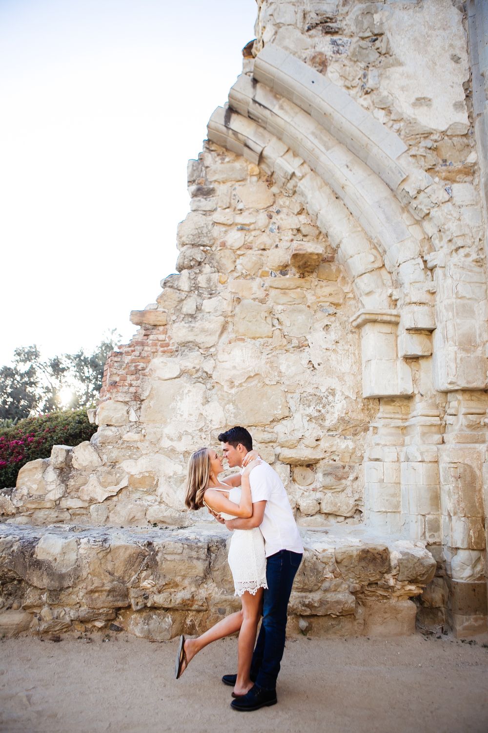 A romantic couple shares tender engagement photos against a weathered stone archway backdrop.