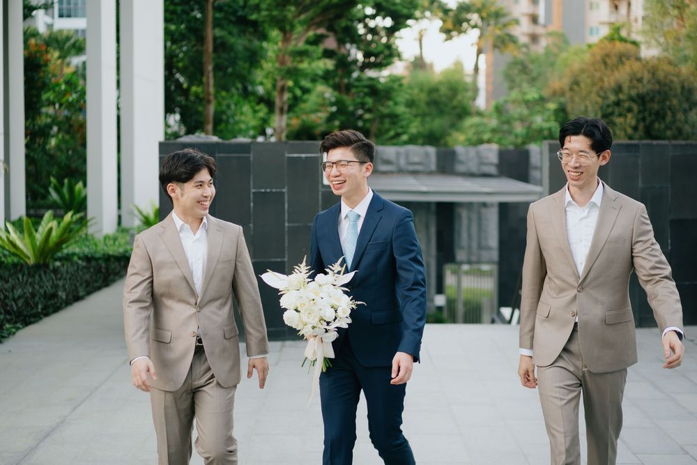 Three people in business attire walk together outdoors, with one holding a white floral bouquet.