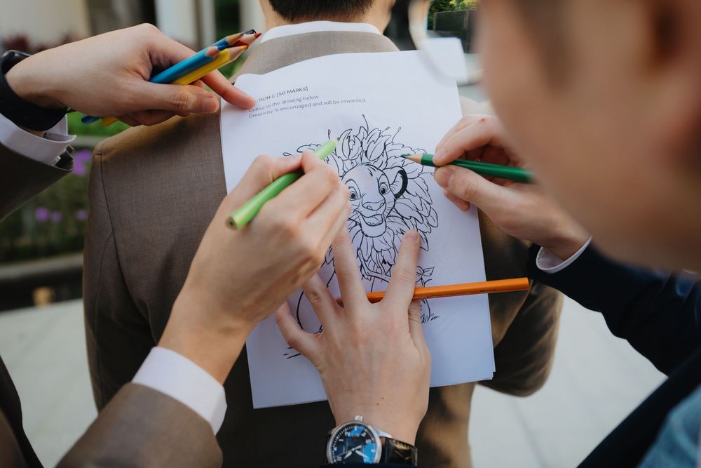 Students coloring and sketching using crayons and colored markers on white paper at a shared table.