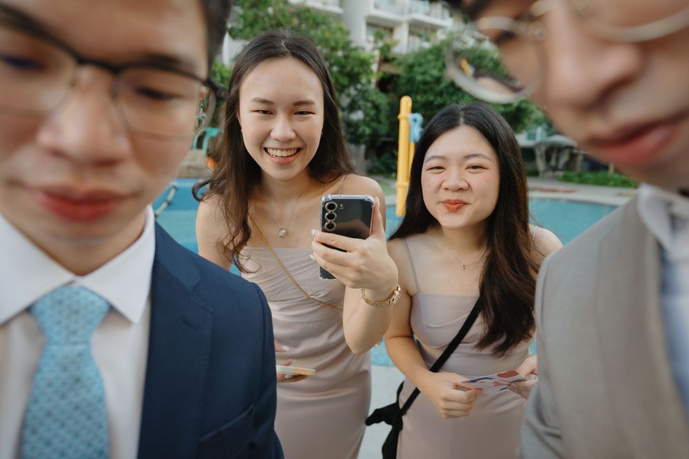 A candid group scene in a bright outdoor setting with smartphones and smiles.