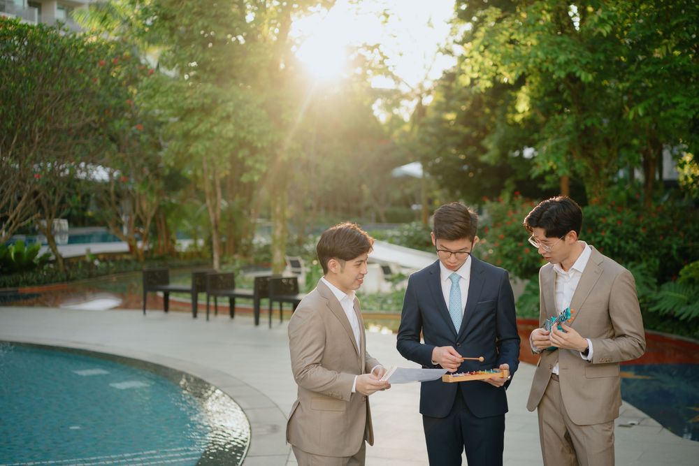 Three business professionals in tan suits review documents together by a pool during golden hour lighting.