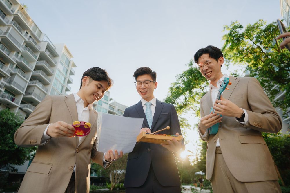 Three businesspeople in beige and grey suits review documents together outdoors near an office building.