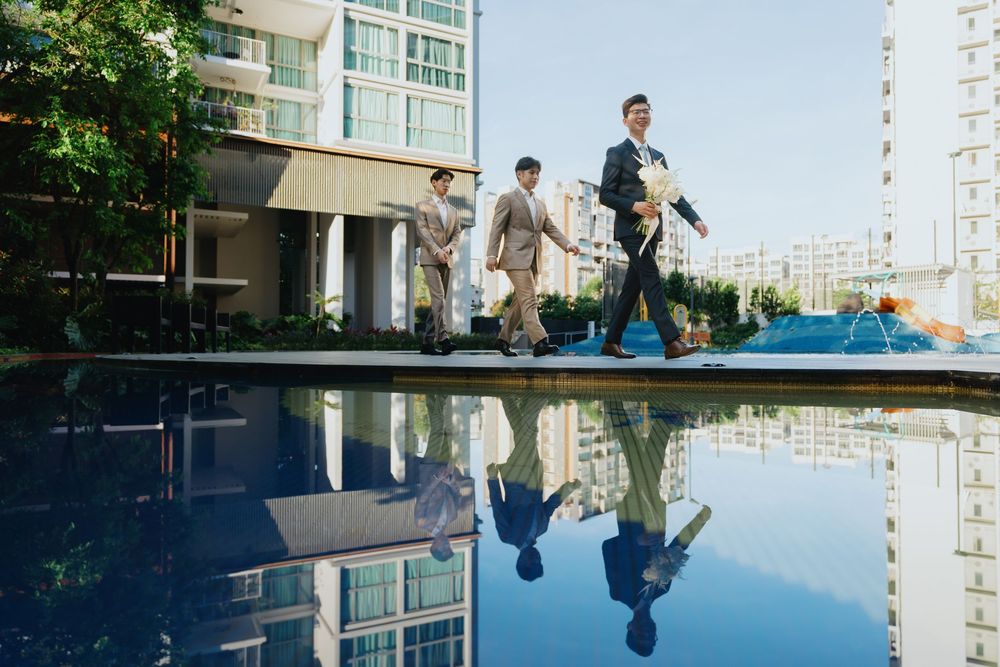 People walk along the edge of a reflective pool with modern apartment buildings in the background.