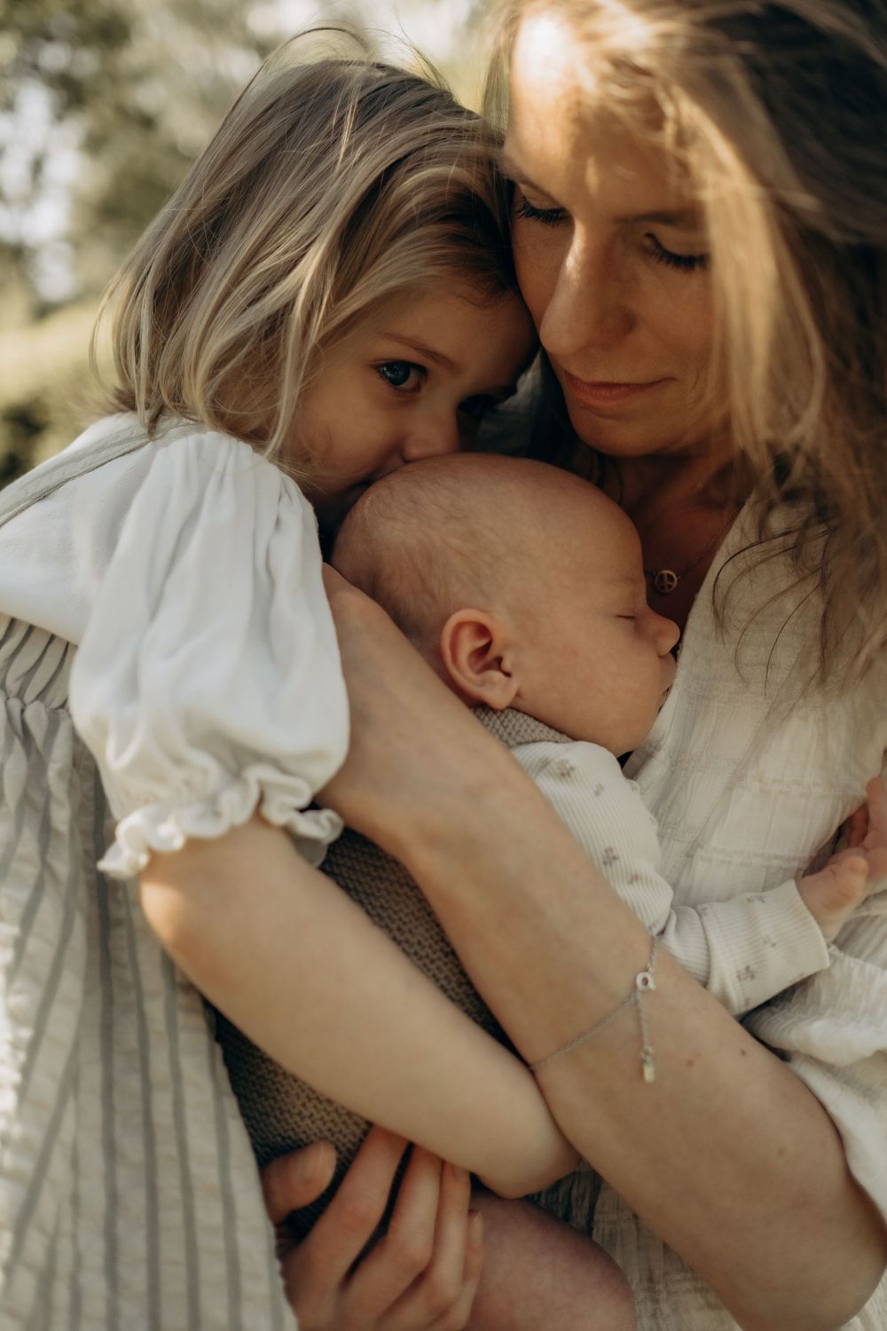 little girl kissing head of her baby sister while mom holds them during candid family photoshoot in Stockholm