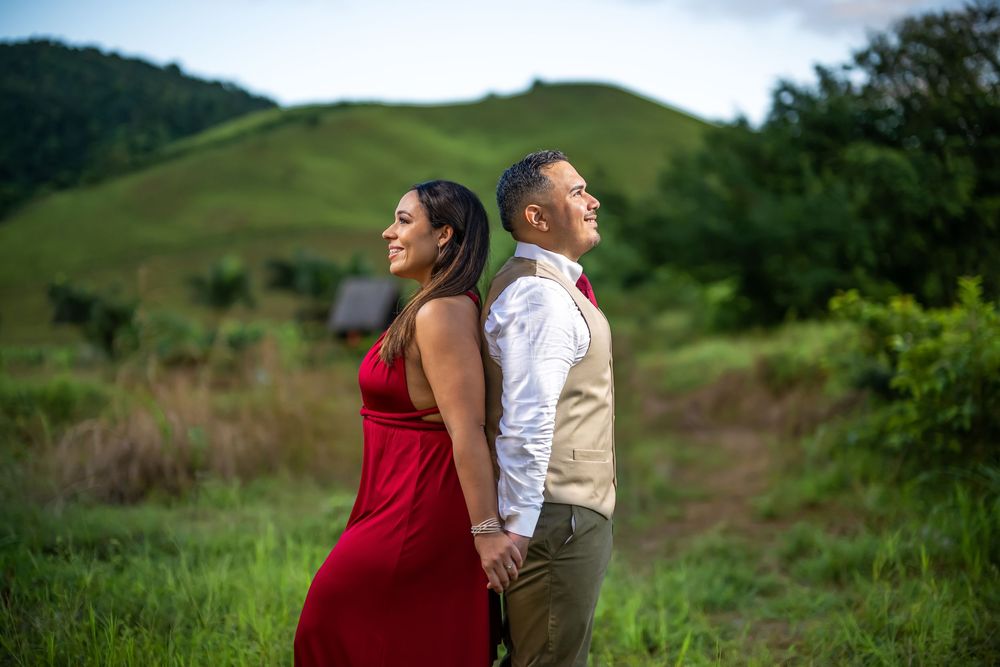 Two people in red dress and khaki outfit holding each other amid rolling green hills on a cloudy afternoon.
