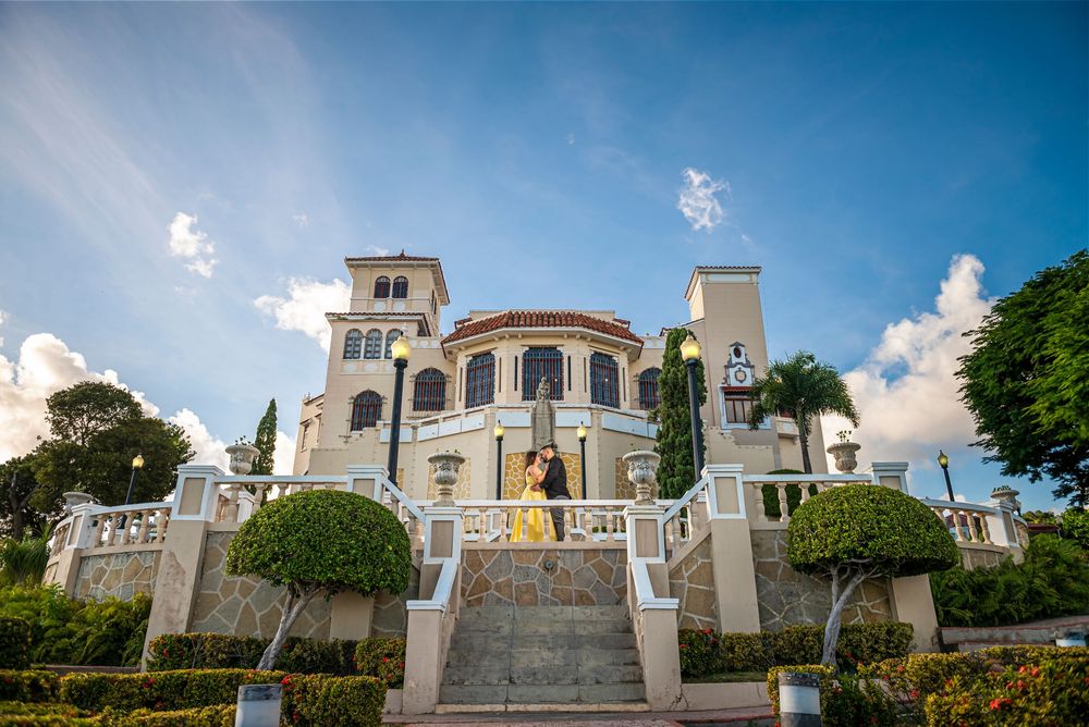 Elegant Mediterranean-style mansion with white towers and grand staircase under blue sky with puffy clouds.
