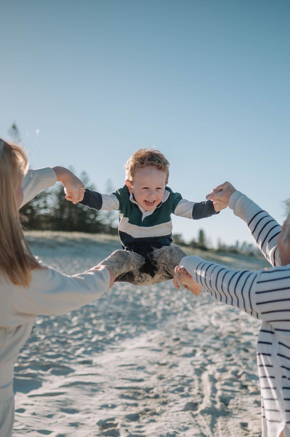 Parent tossing and playing with a child on a sunny beach with waves and blue sky in the background.
