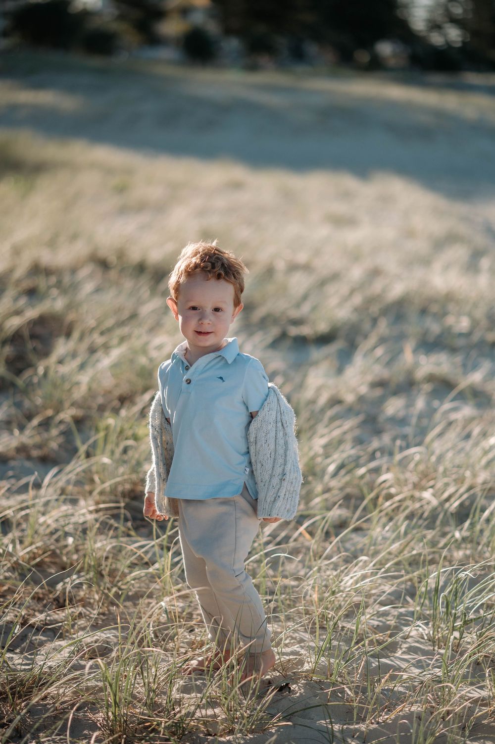 Small child standing in tall grass wearing light colored clothing during golden hour at sunset.