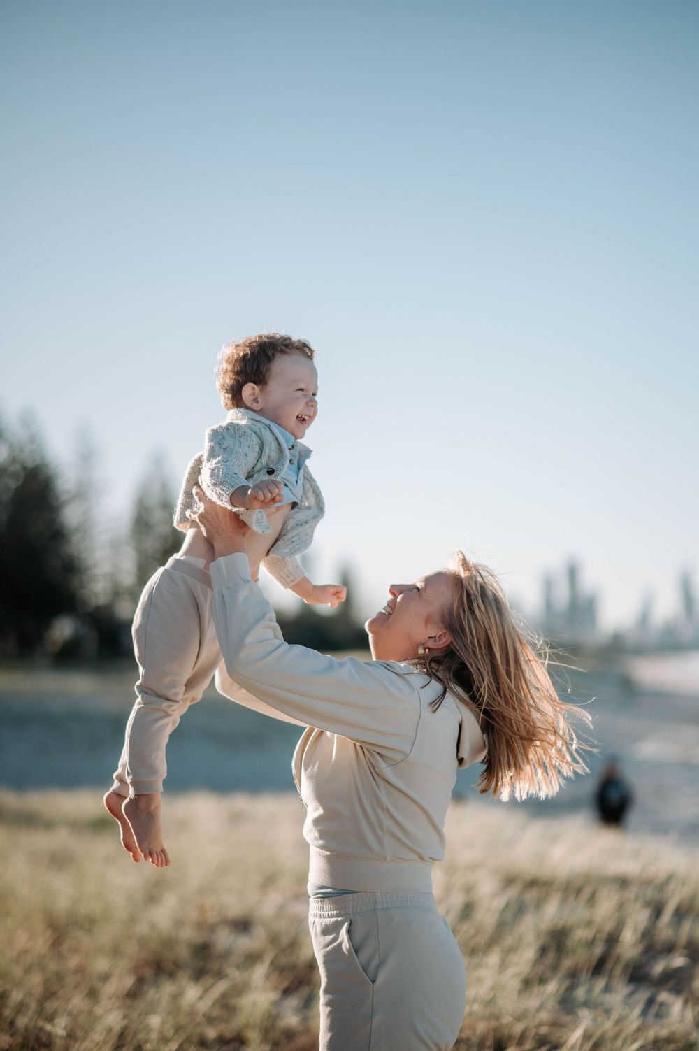 Playful moment captured in a field as parent lifts small child against blue sky.