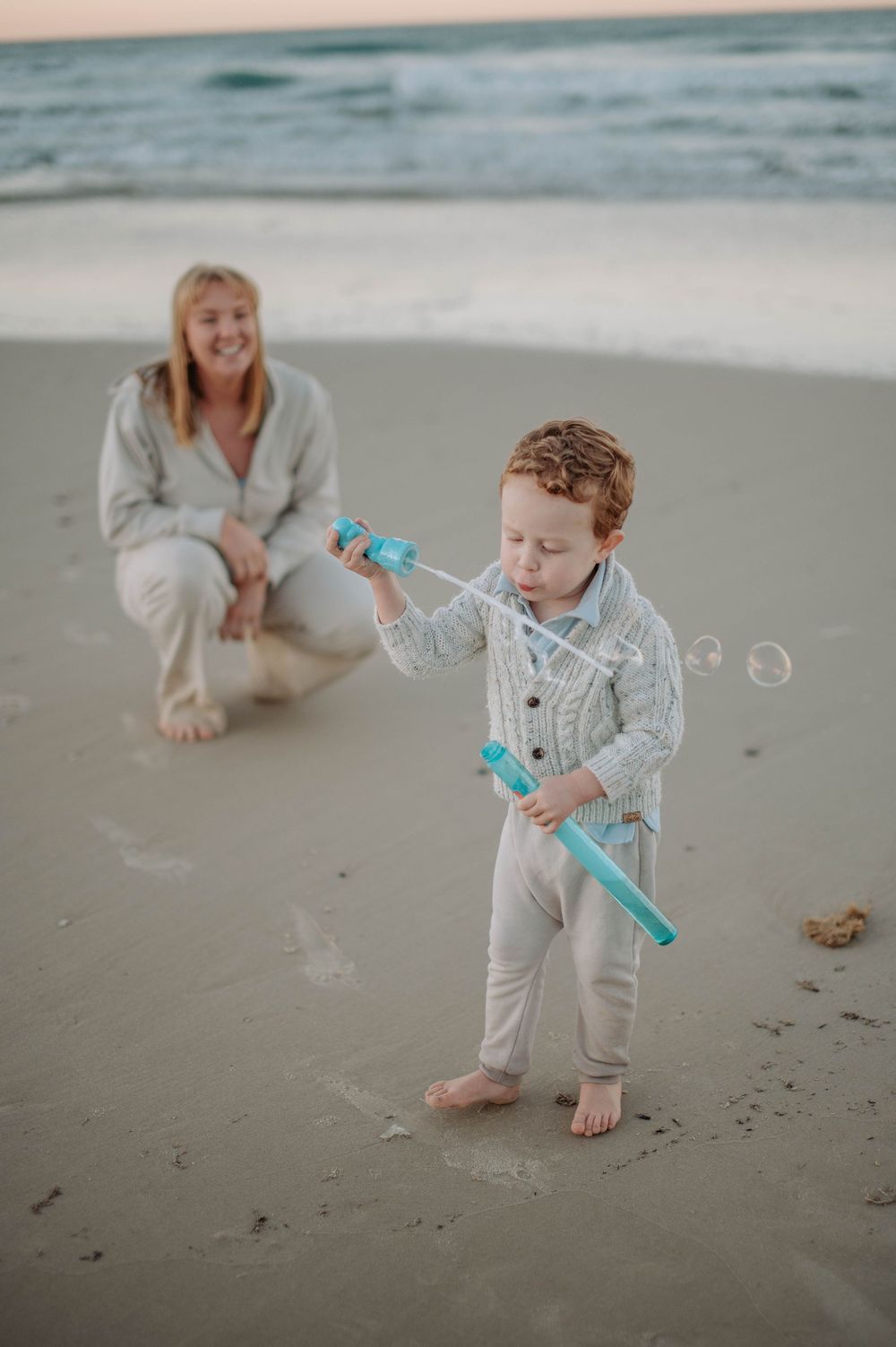 Children playing with bubbles on a misty beach in white outfits during a casual family photoshoot.
