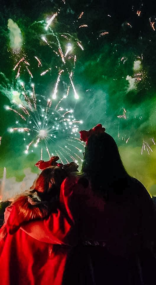 Silhouettes watch bright green fireworks explode in the night sky.