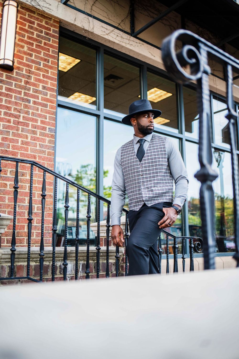Stylish outfit featuring grey vest, hat and tie against brick building exterior.