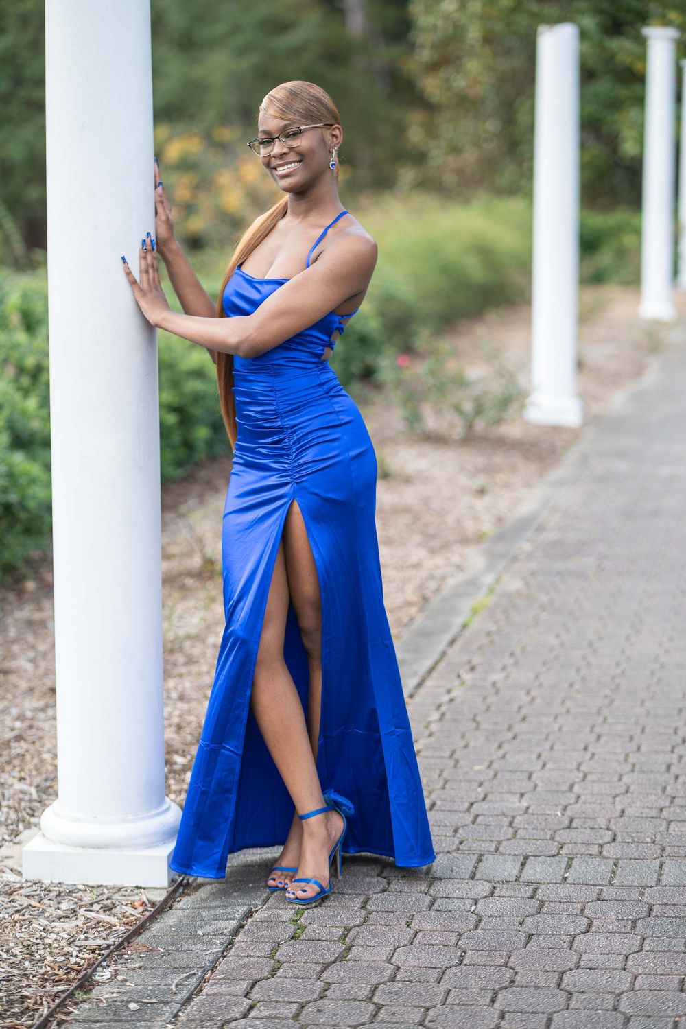 Elegant royal blue evening gown with thigh-high slit and matching heels posed by white column.