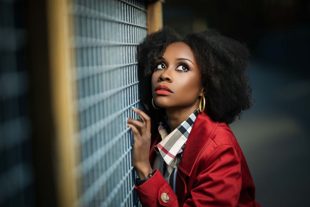 Fashion portrait in red coat and plaid scarf against industrial backdrop.