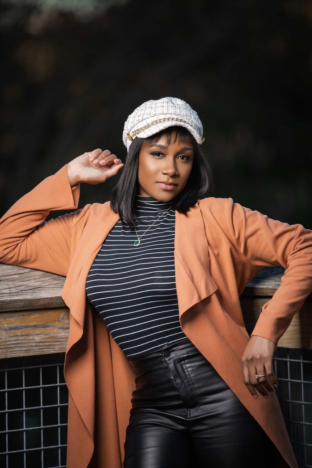 Fashion portrait showcasing peach coat, striped top and newsboy cap in outdoor setting.