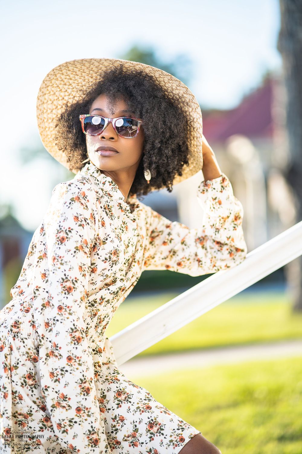 Summer boho style with floral dress, wide-brim straw hat and sunglasses in golden sunlight.