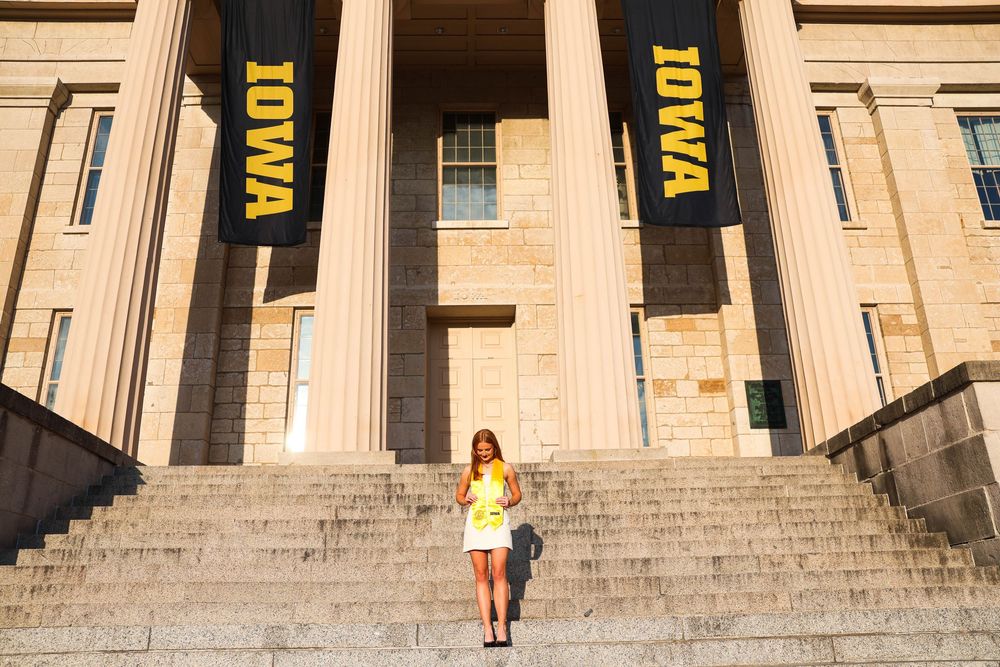 A student stands on stone steps between large black banners at an Iowa campus building entrance.
