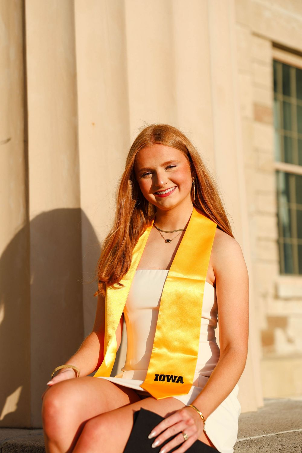 Graduate in yellow and white outfit poses on stone steps during golden hour photography session.