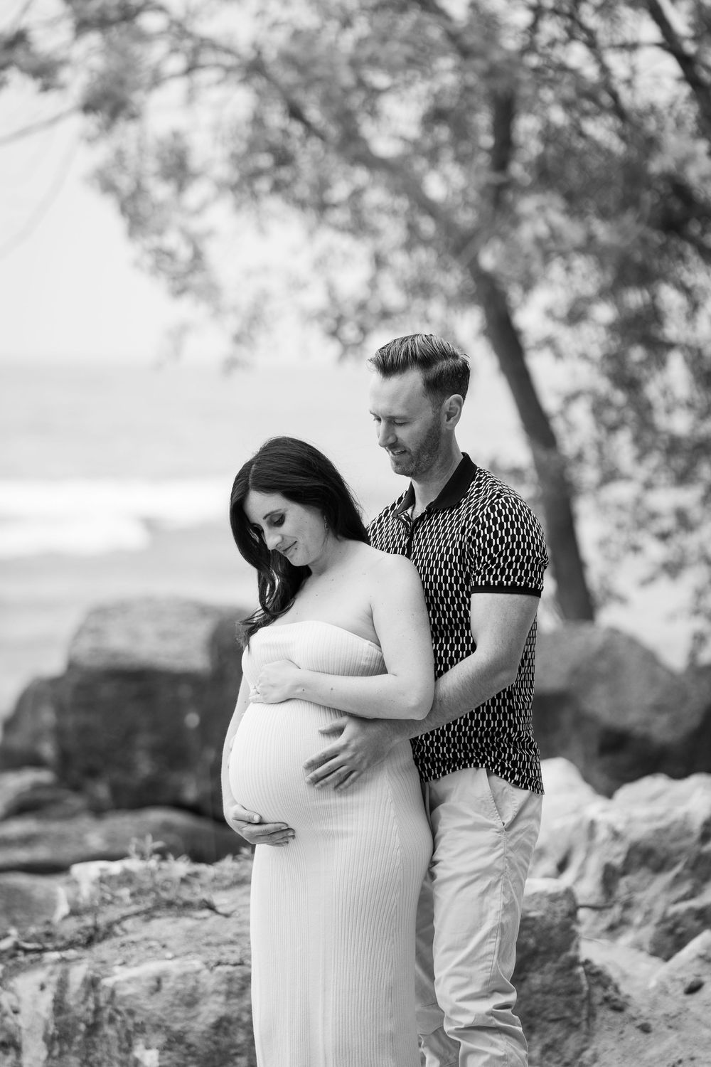 Black and white maternity photos showing a couple embracing on rocky terrain in a romantic outdoor setting.